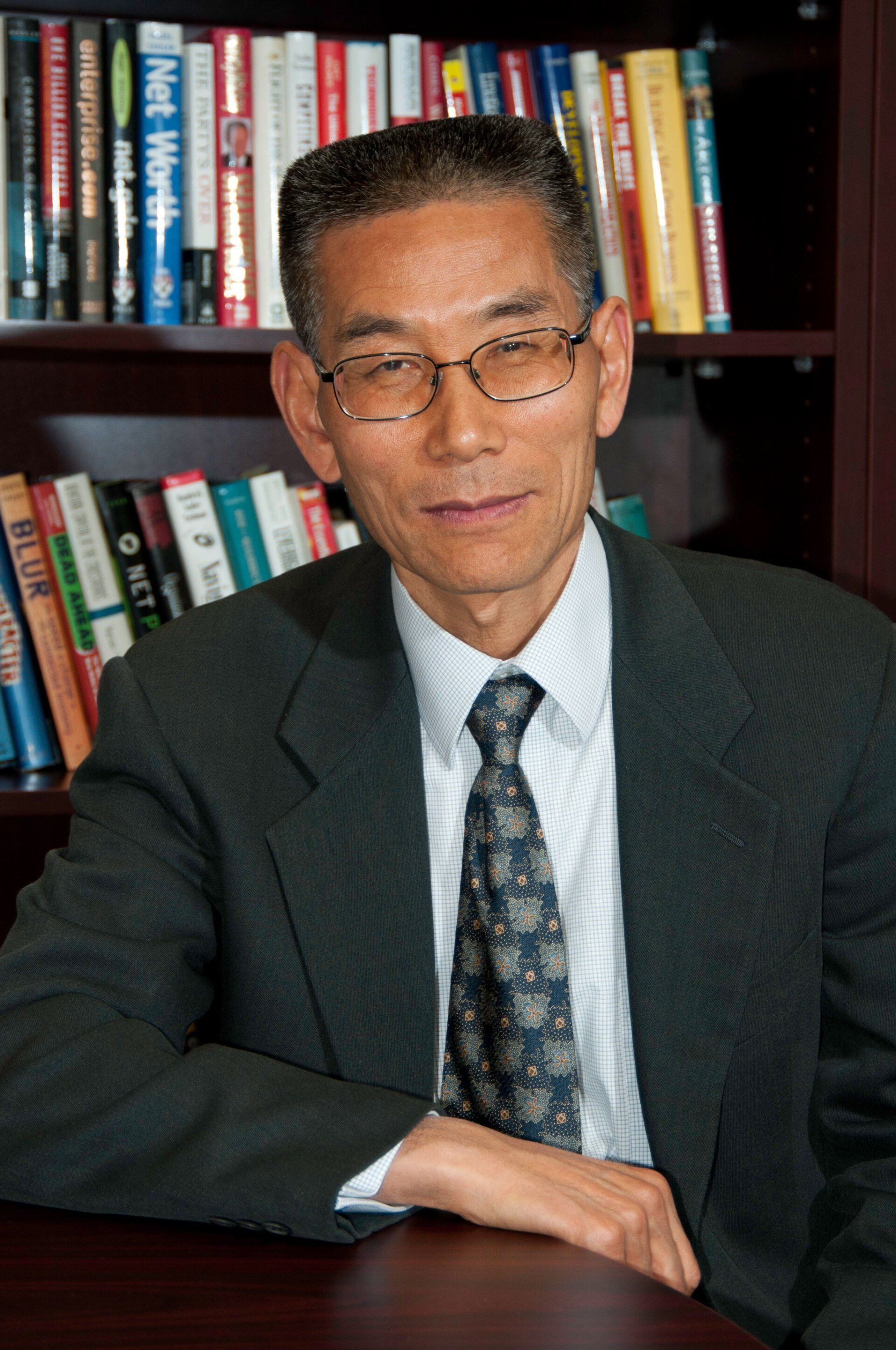 A man in a suit and tie is sitting in front of a bookshelf