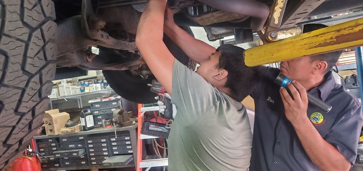 Two men are working under a car in a garage.
