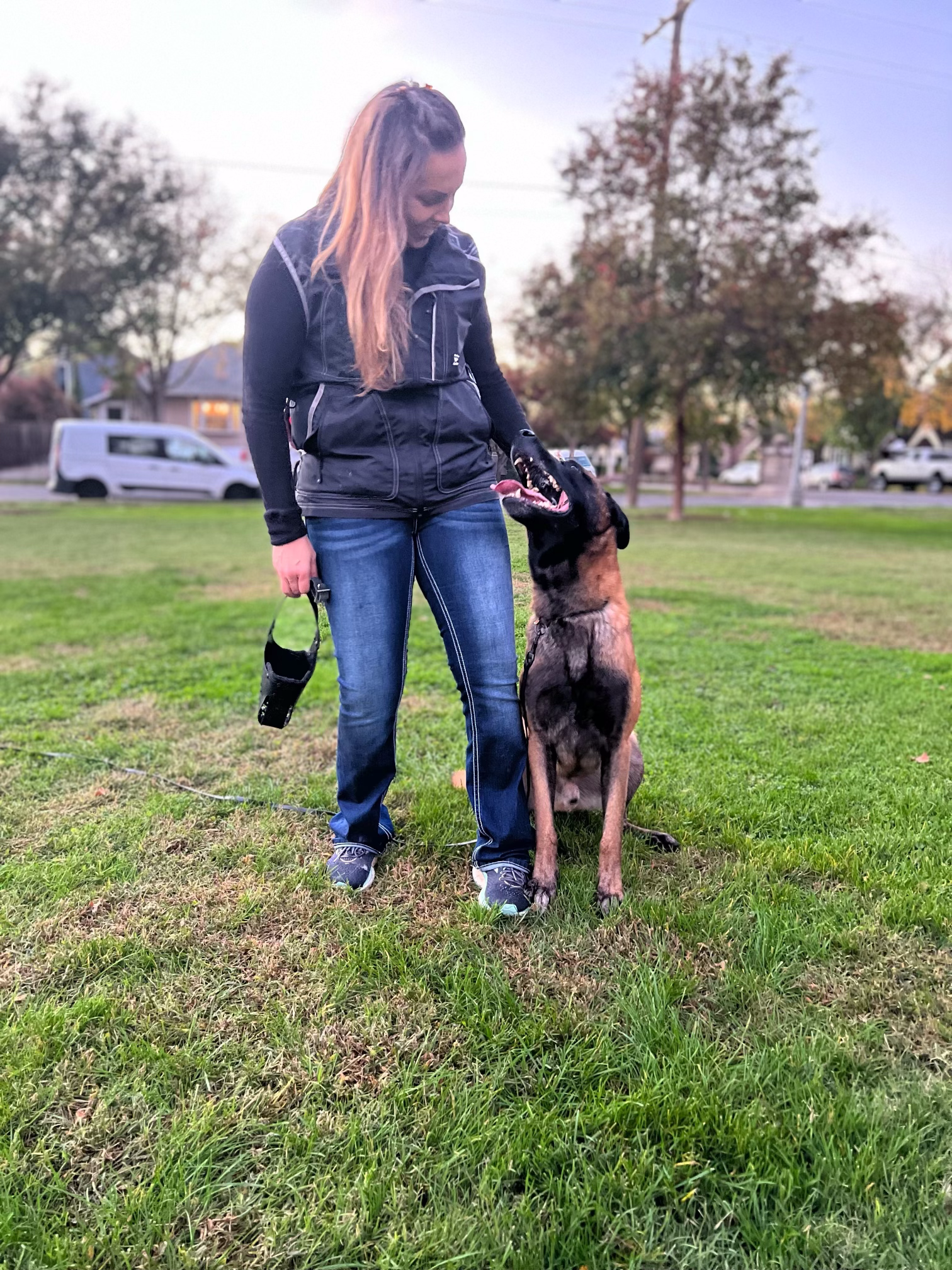 a woman is standing next to a dog in a park .