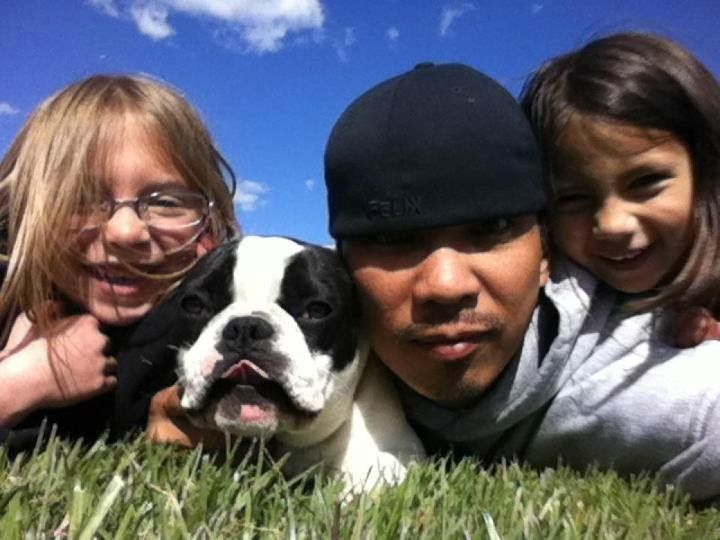 a man and two girls pose with a dog in the grass