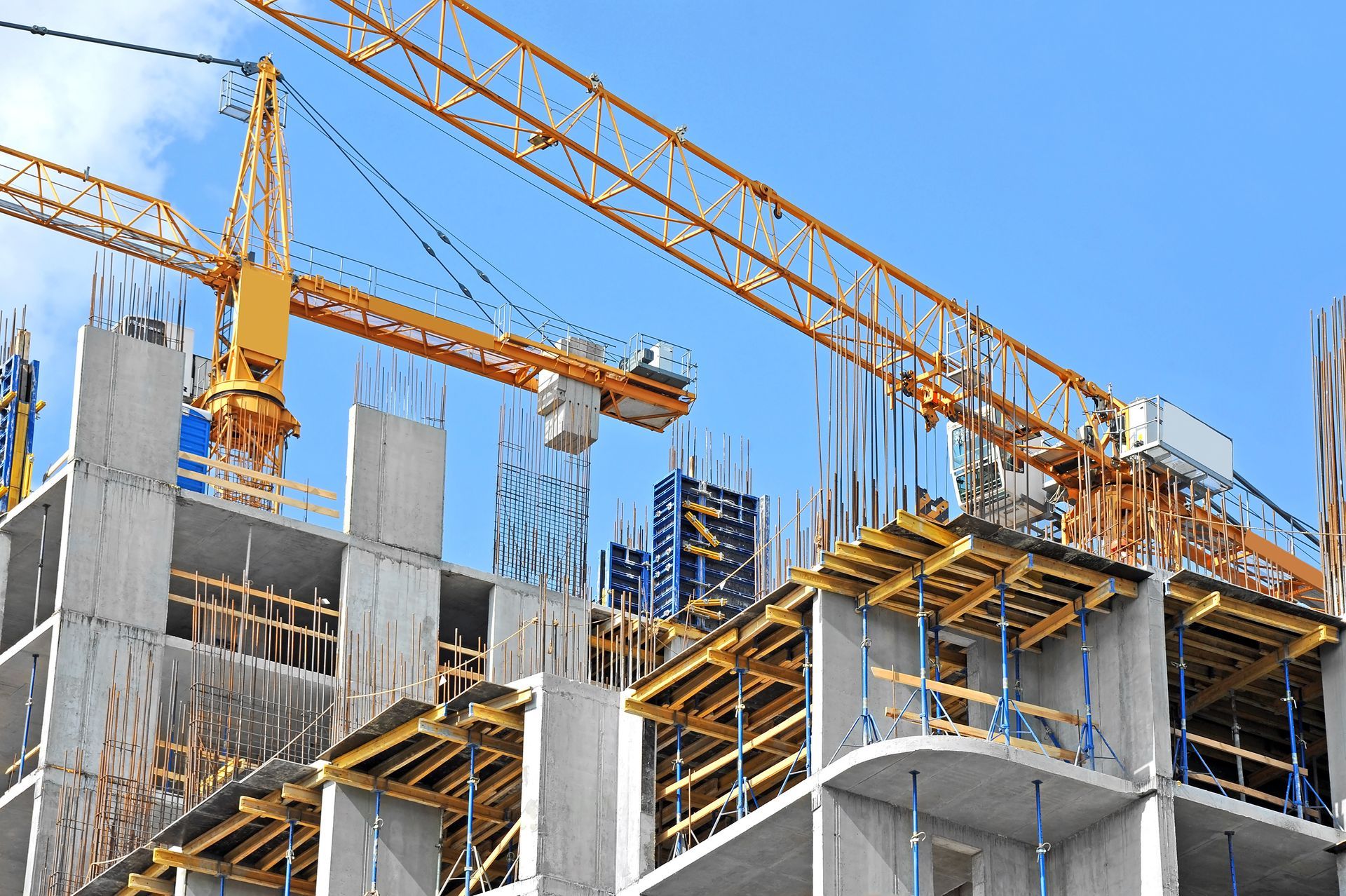 Construction site with a yellow crane, concrete framework, and blue sky.
