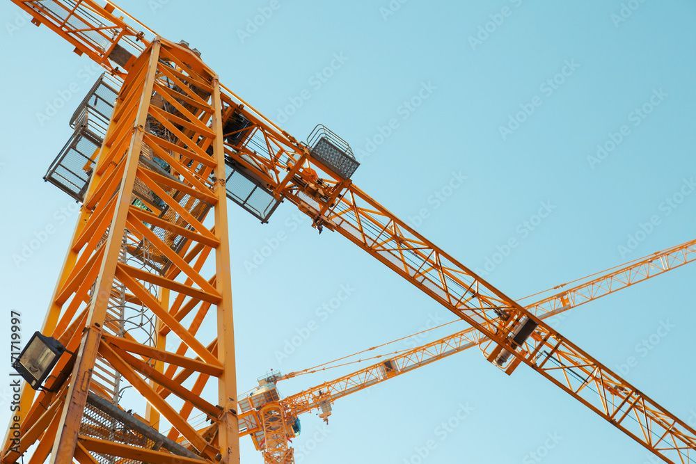 Yellow construction cranes against a clear blue sky.