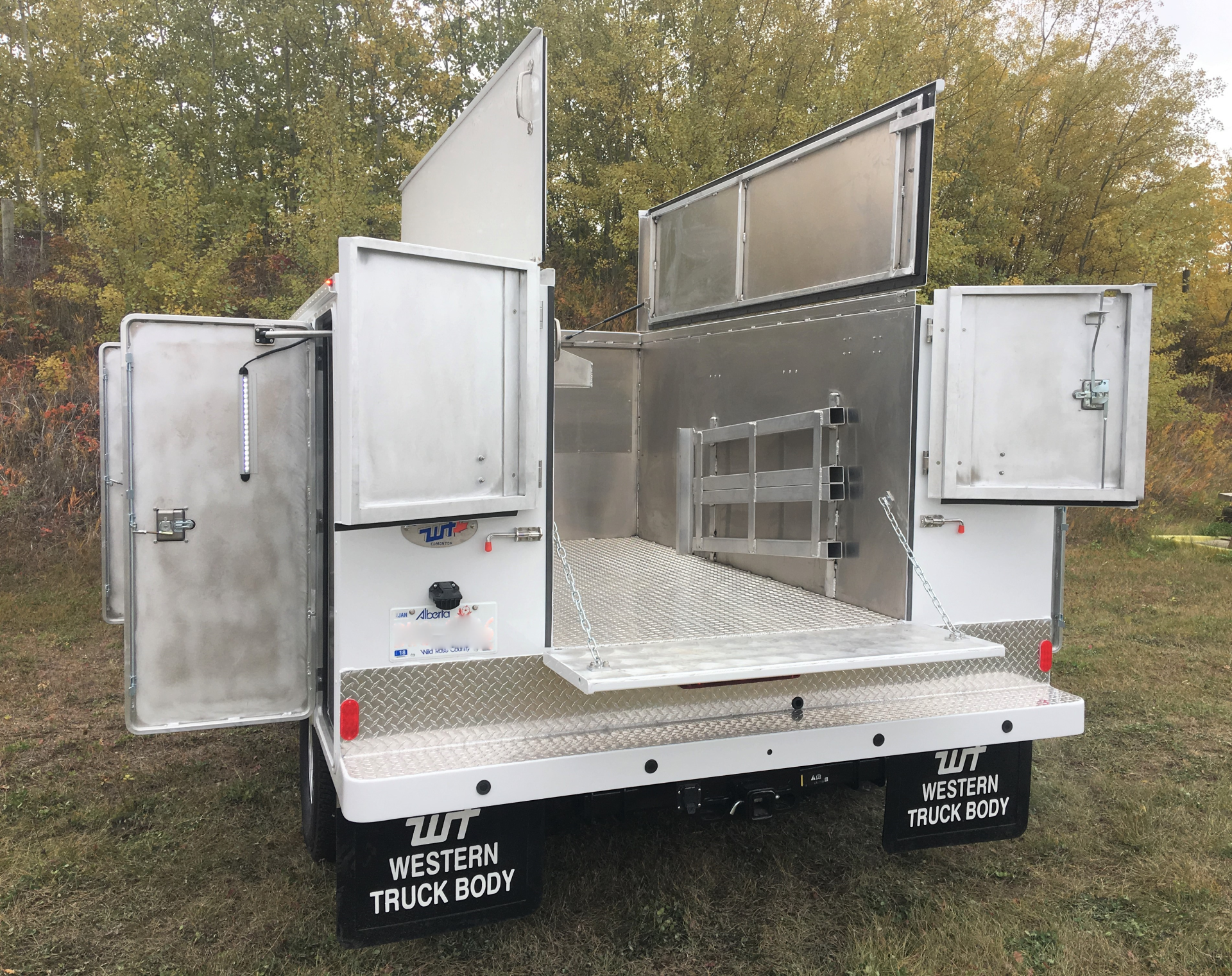White utility truck with multiple open doors, revealing storage compartments, parked outdoors.