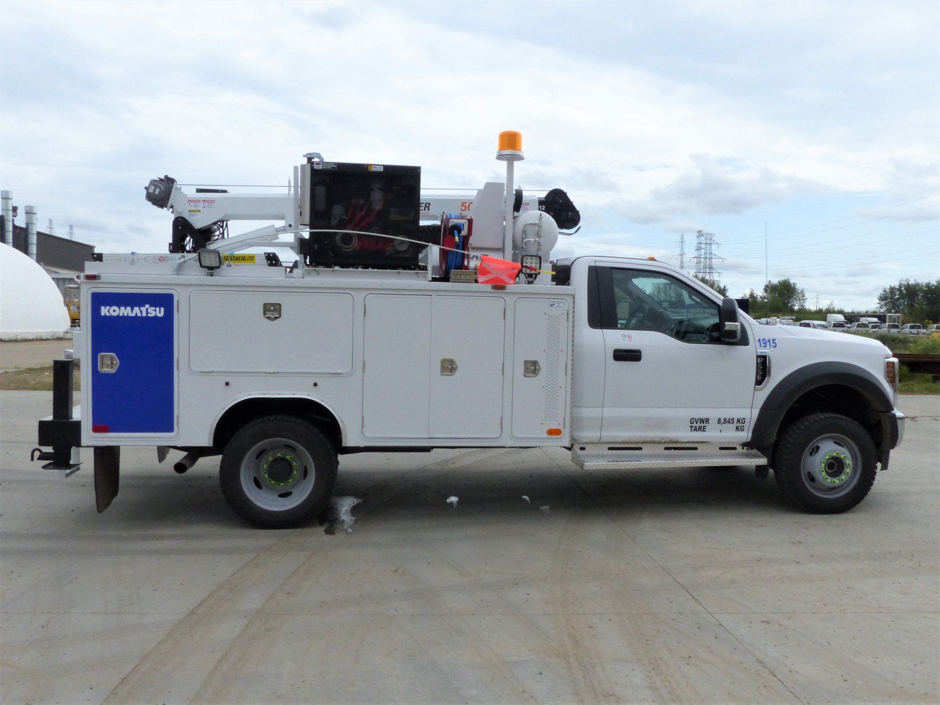 White utility truck with crane and storage compartments on a paved surface.
