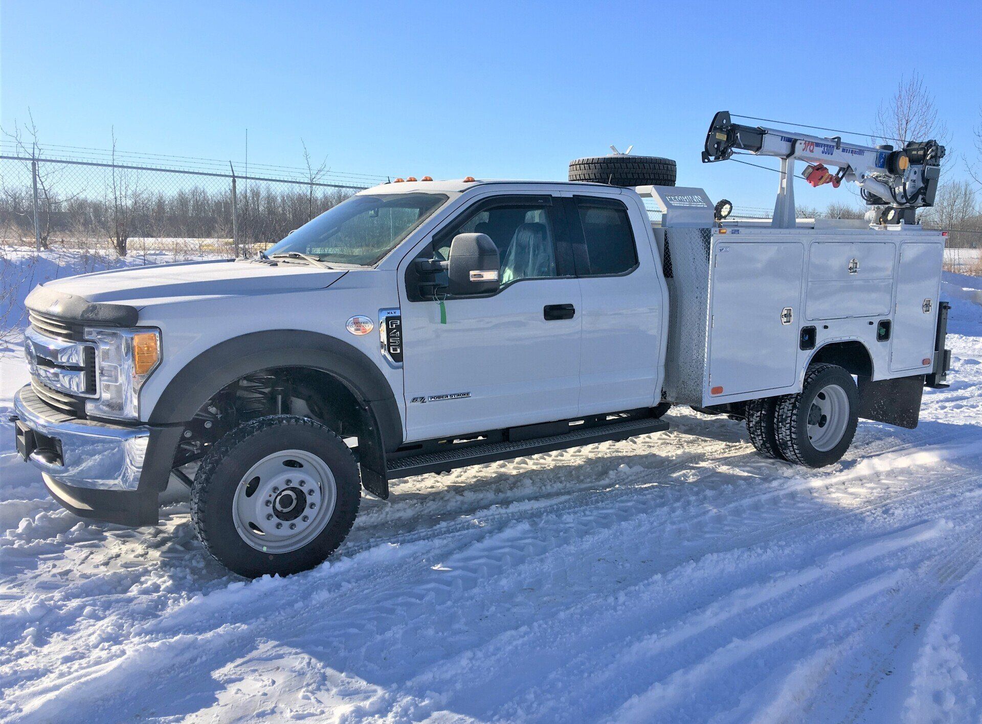 White work truck with crane parked in snow, sunny day.