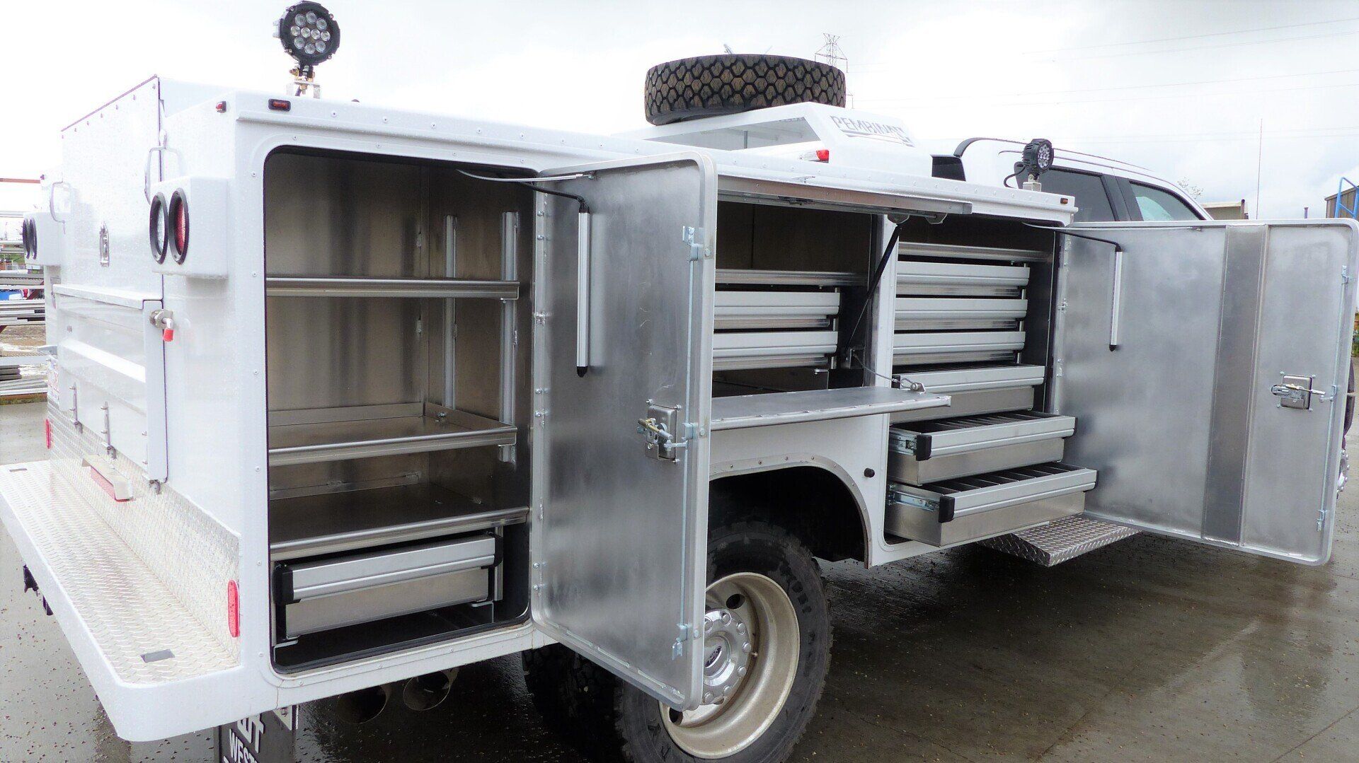 A white utility service truck with open side storage compartments revealing metal shelves and drawers.