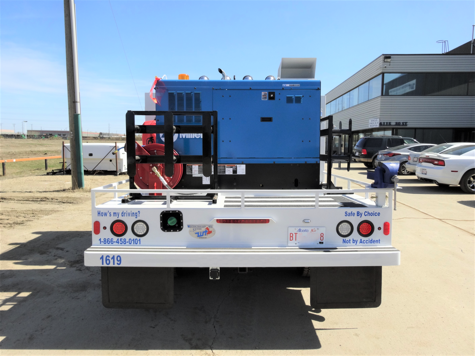 Blue generator on white flatbed truck, parked outdoors near buildings.