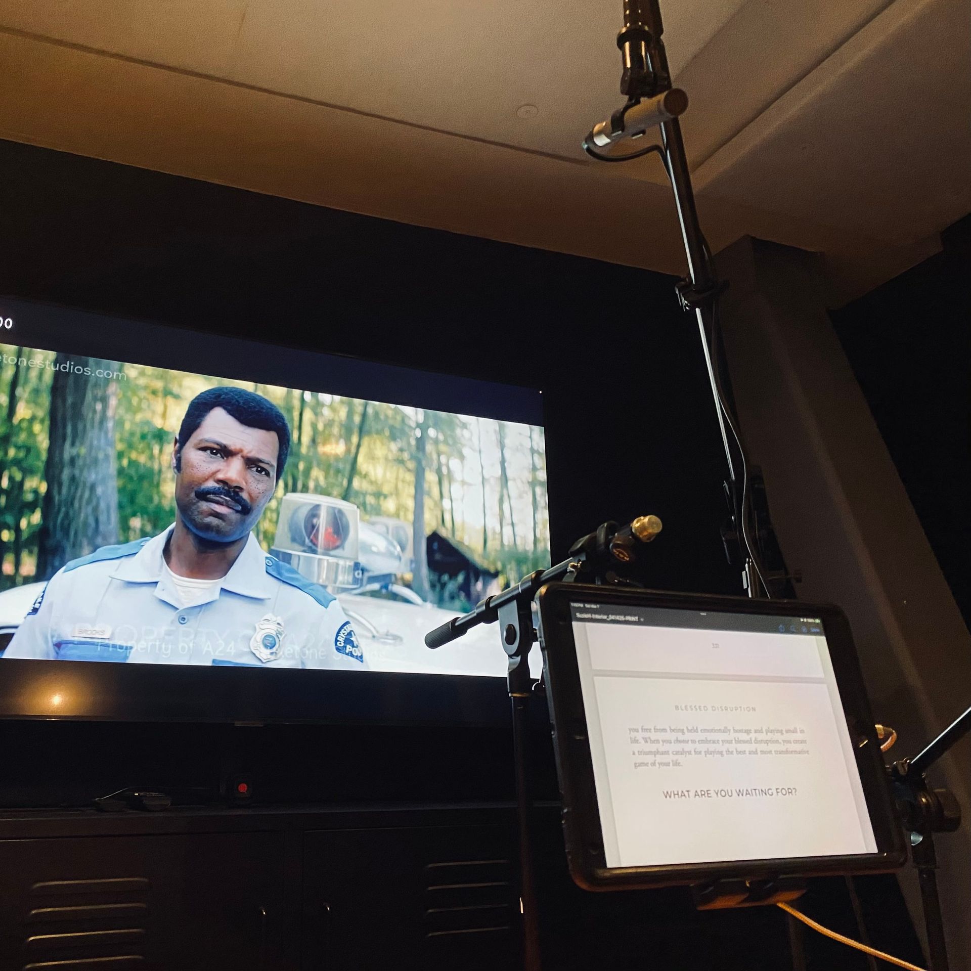 A person in a police uniform on a screen next to a tablet on a stand, likely being used for voice-over recording.