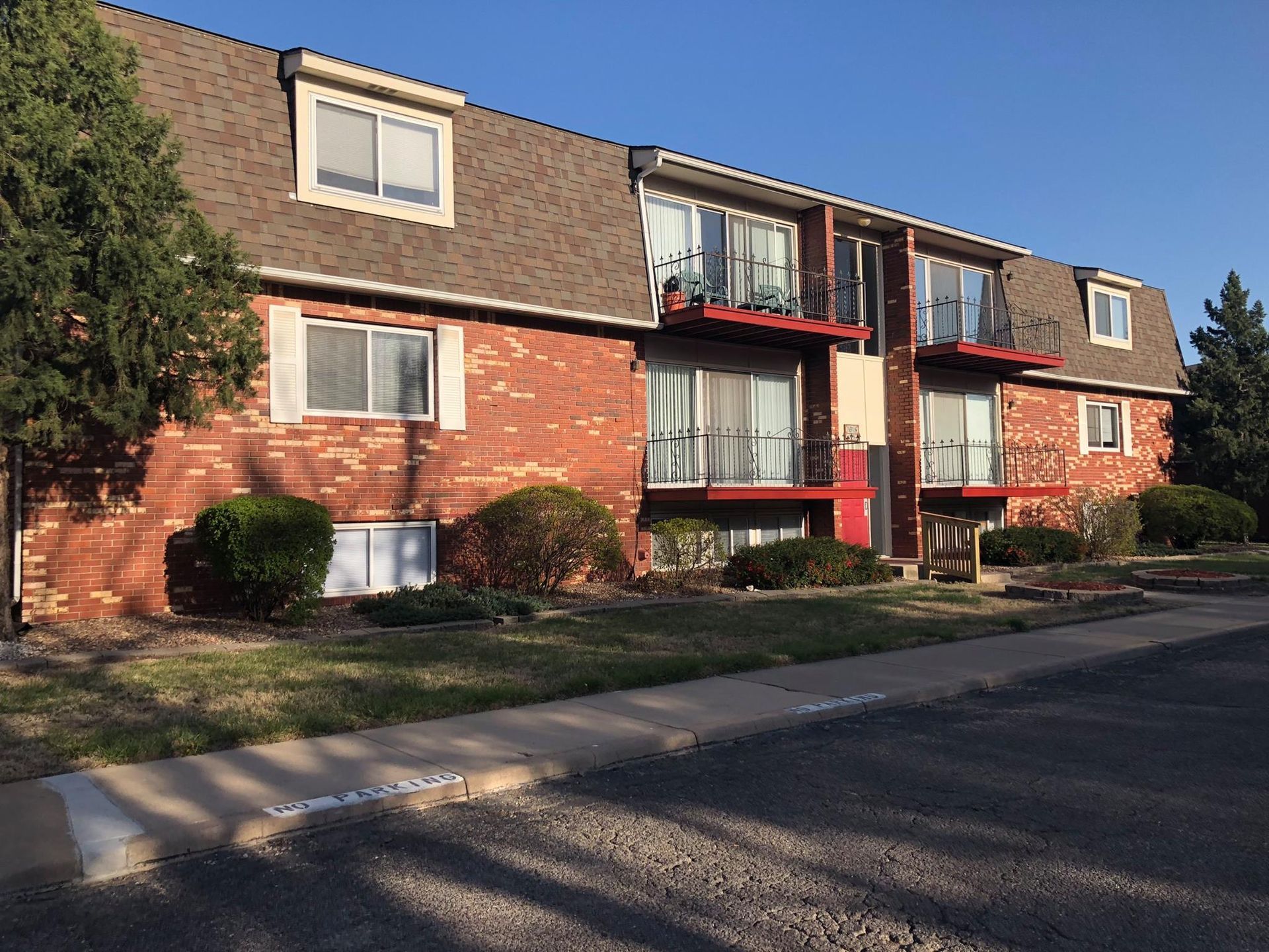 Red brick apartment building with brown roof and small balconies.