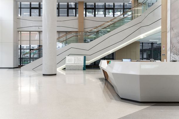 Bright modern atrium with escalators, white floors, large windows, and a reception desk
