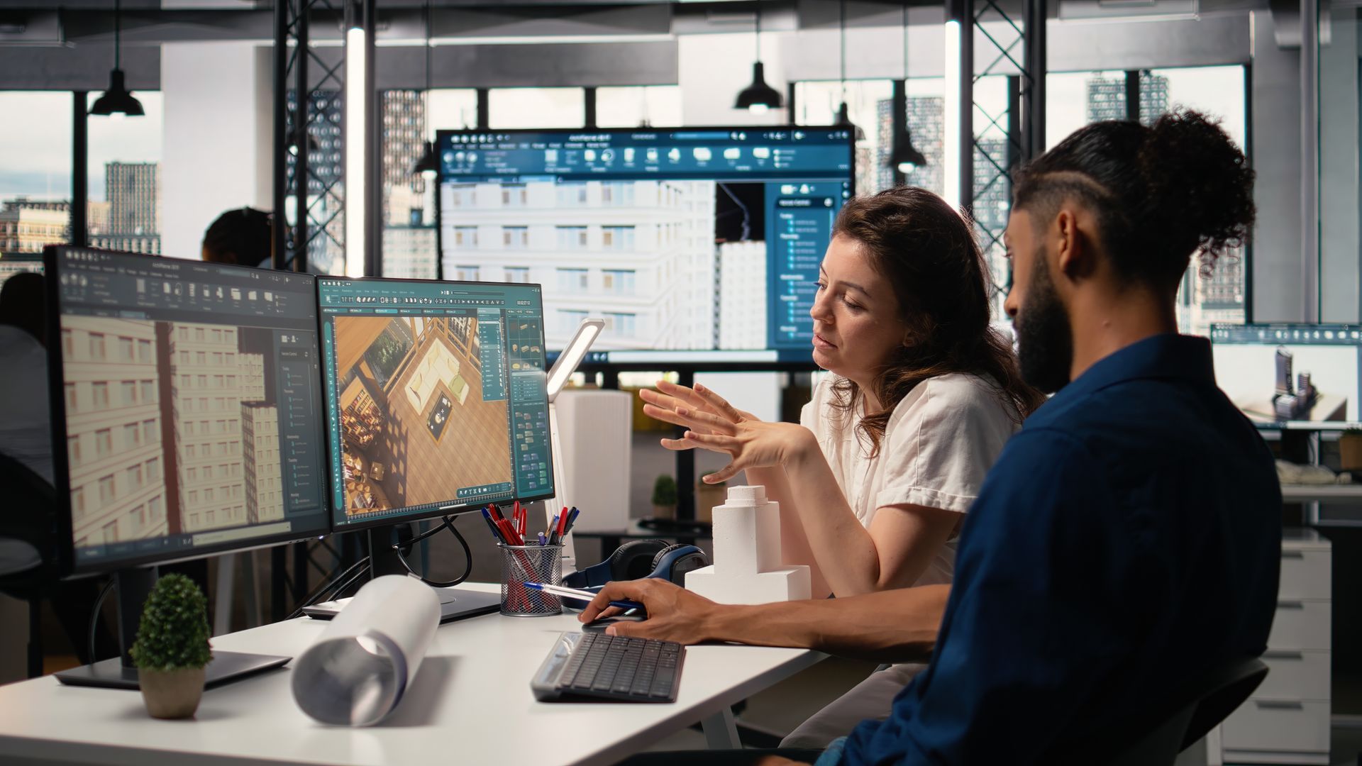 Two coworkers collaborating at a desk with multiple monitors in a modern office Two coworkers collaborating at a desk with multiple monitors in a modern office