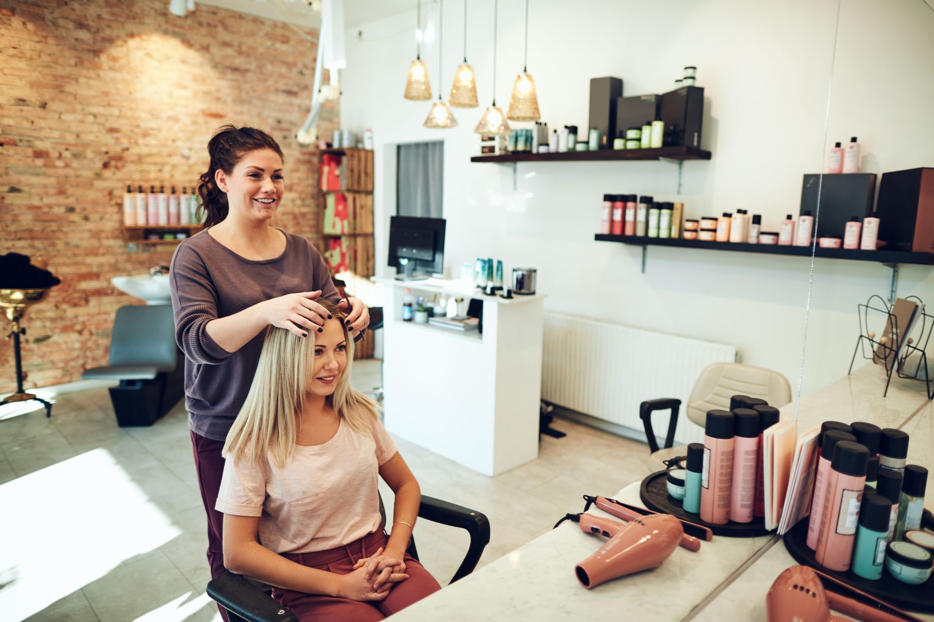 Hairdresser styling a smiling client’s hair in a bright salon with styling tools on the counter