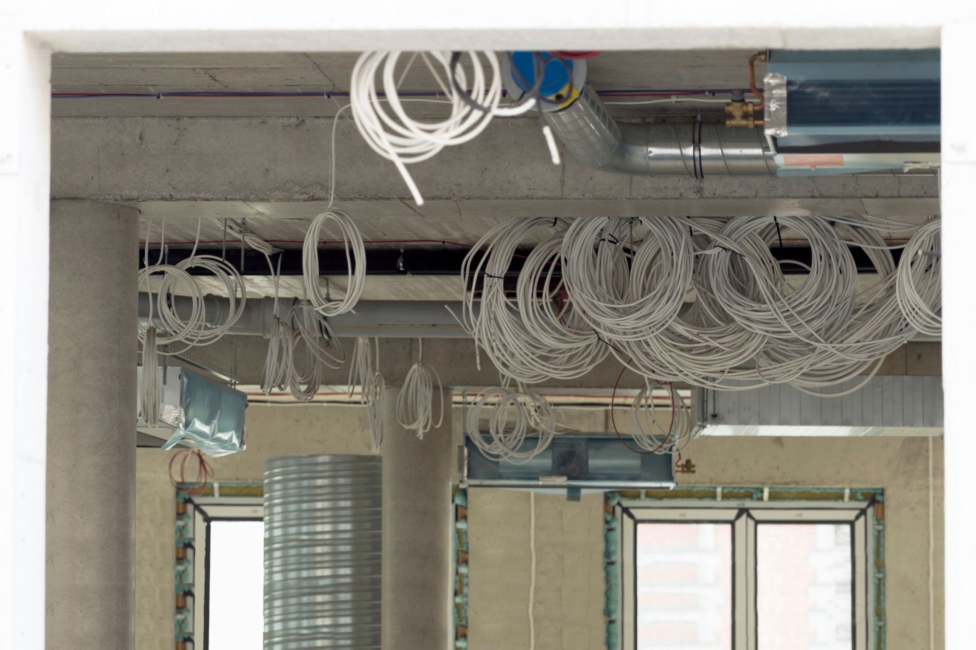 Unfinished room ceiling with exposed wiring and HVAC ducts over windows and concrete columns