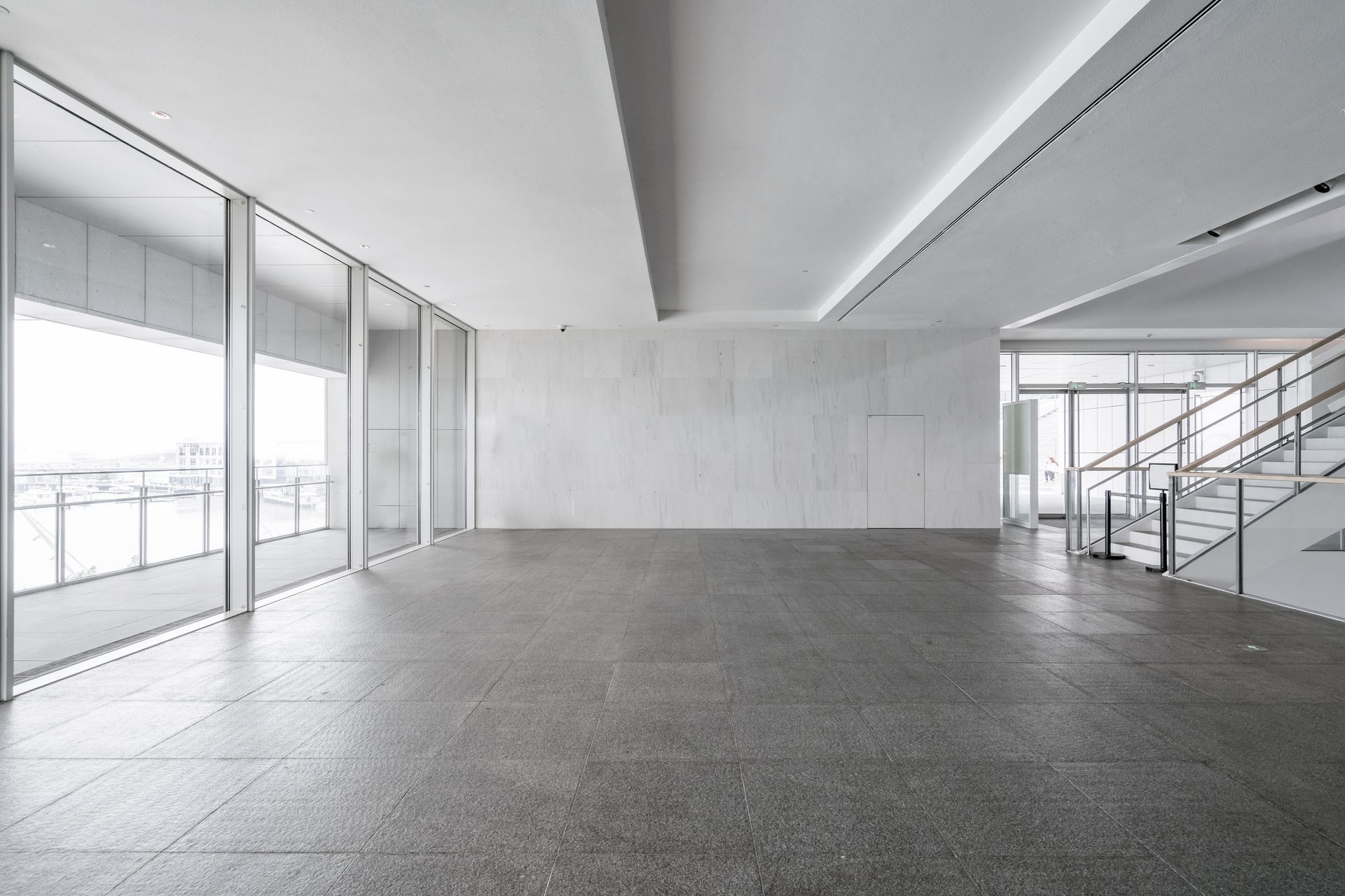 Empty modern office with large windows, concrete floor, and staircase on the right Empty modern office with large windows, concrete floor, and staircase on the right