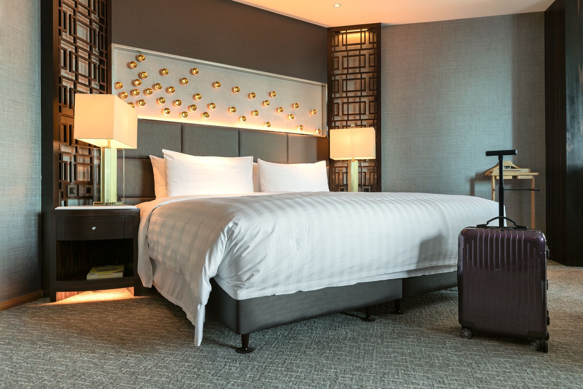 Modern hotel room with a neatly made bed, bedside lamps, and a suitcase on the floor Modern hotel room with a neatly made bed, bedside lamps, and a suitcase on the floor