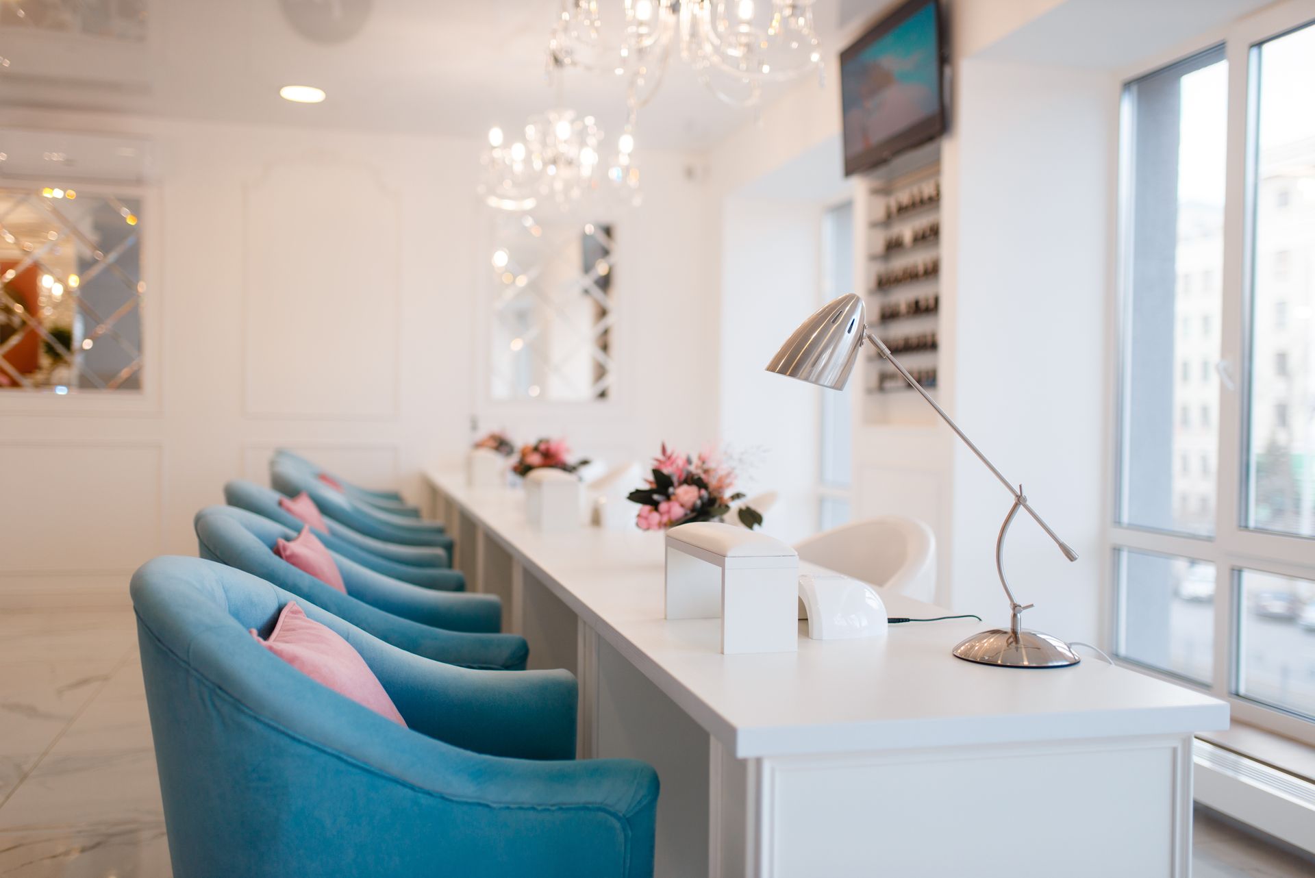 Bright white salon with teal chairs lined along a manicure bar near large windows Bright white salon with teal chairs lined along a manicure bar near large windows