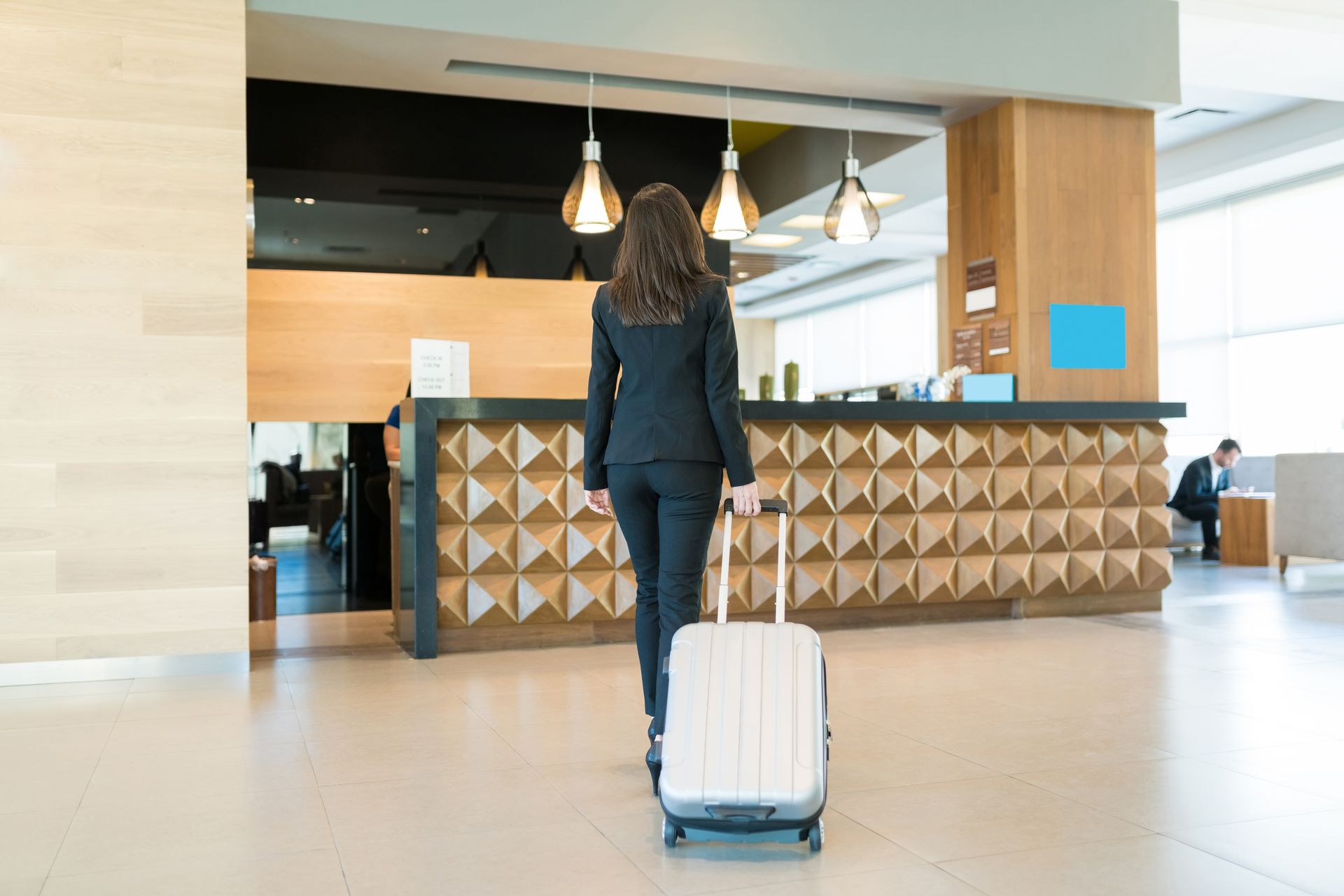 Traveler rolling a white suitcase toward a modern hotel or lobby reception desk