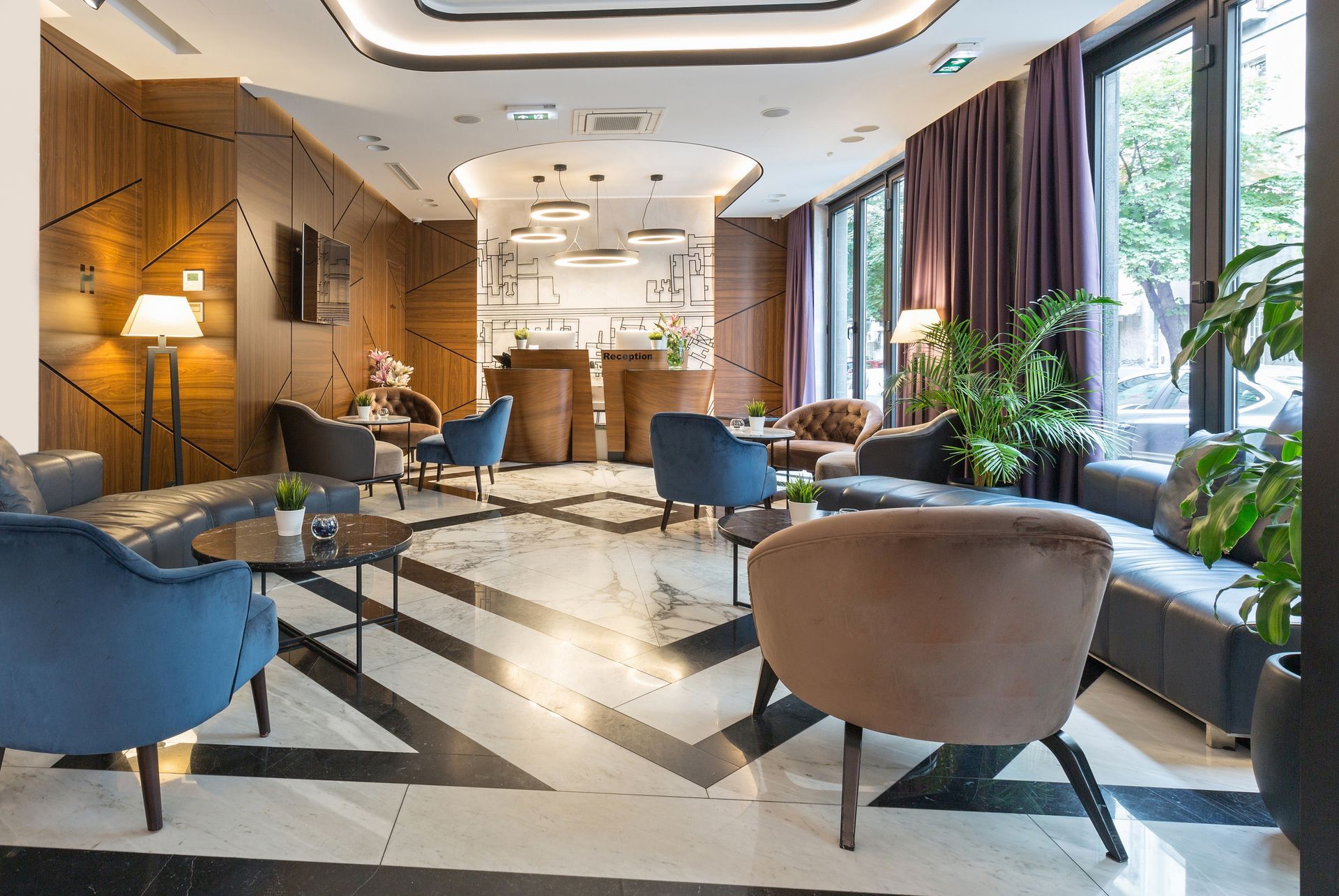 Modern hotel lounge with blue and beige chairs, marble floor, and large windows overlooking greenery Modern hotel lounge with blue and beige chairs, marble floor, and large windows overlooking greenery