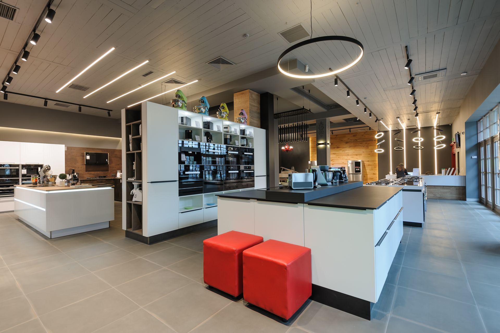 Modern electronics store interior with white display counters, wall screens, and red ottomans