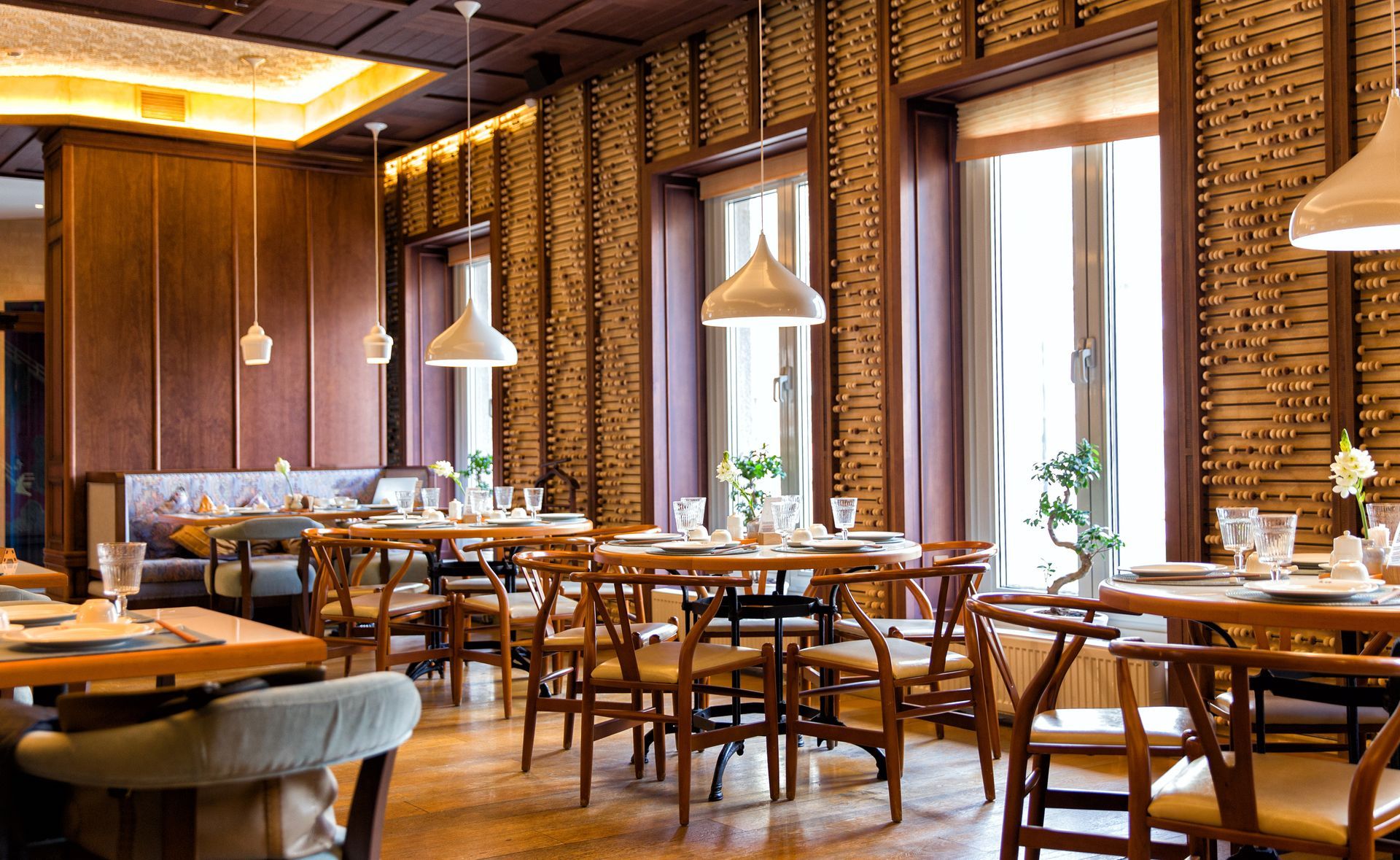 Warm restaurant interior with wooden tables, pendant lights, and brick walls by tall windows