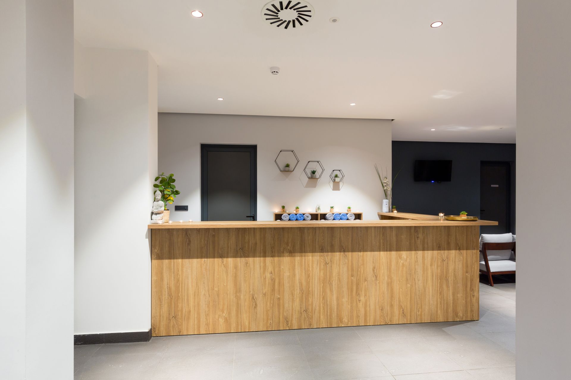 Modern lobby with a wooden reception desk, white walls, recessed lights, and a wall-mounted TV.