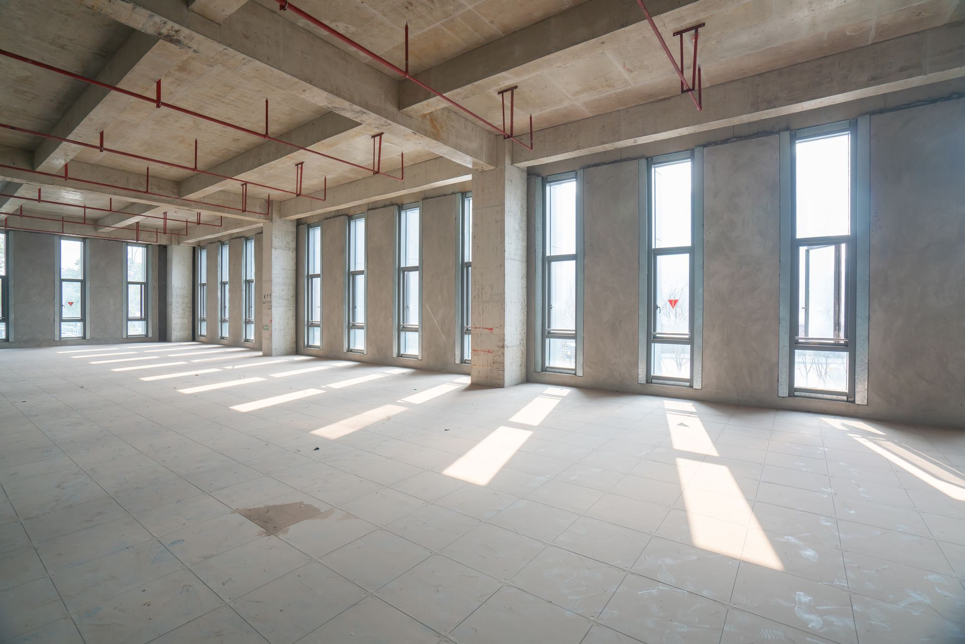 Empty unfinished concrete room with tall windows and sunlight streaming across the floor