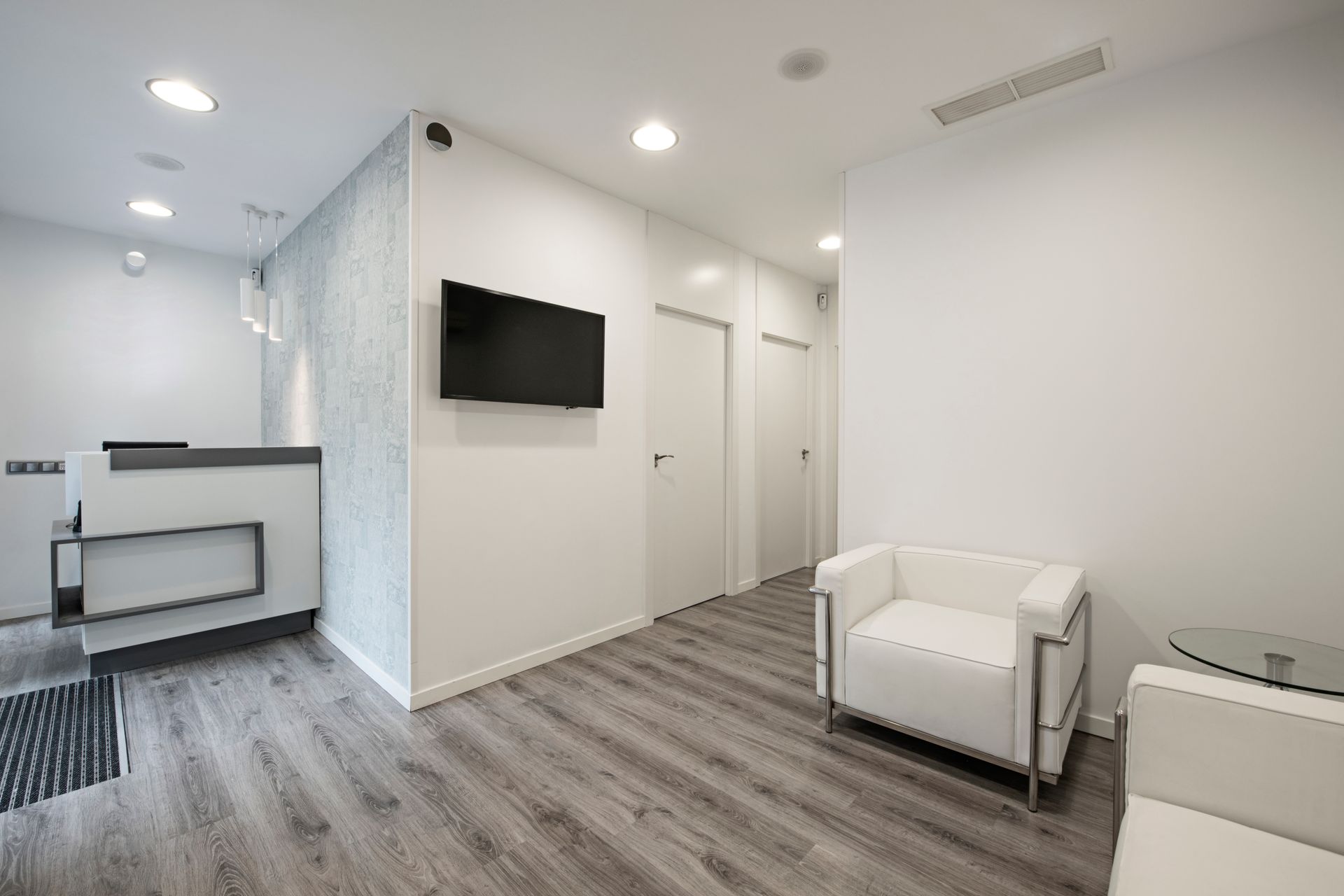 Modern white office waiting area with TV, desk nook, chairs, and gray wood flooring Modern white office waiting area with TV, desk nook, chairs, and gray wood flooring