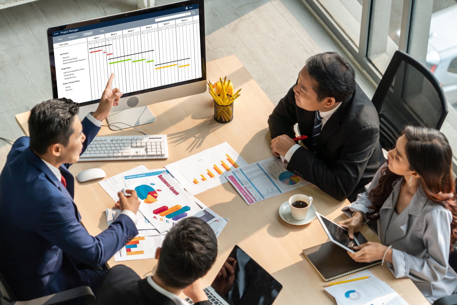 Business team in a meeting reviewing charts on a large monitor and documents around a desk