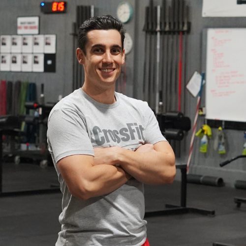 A man wearing a crossfit shirt is standing in a gym with his arms crossed