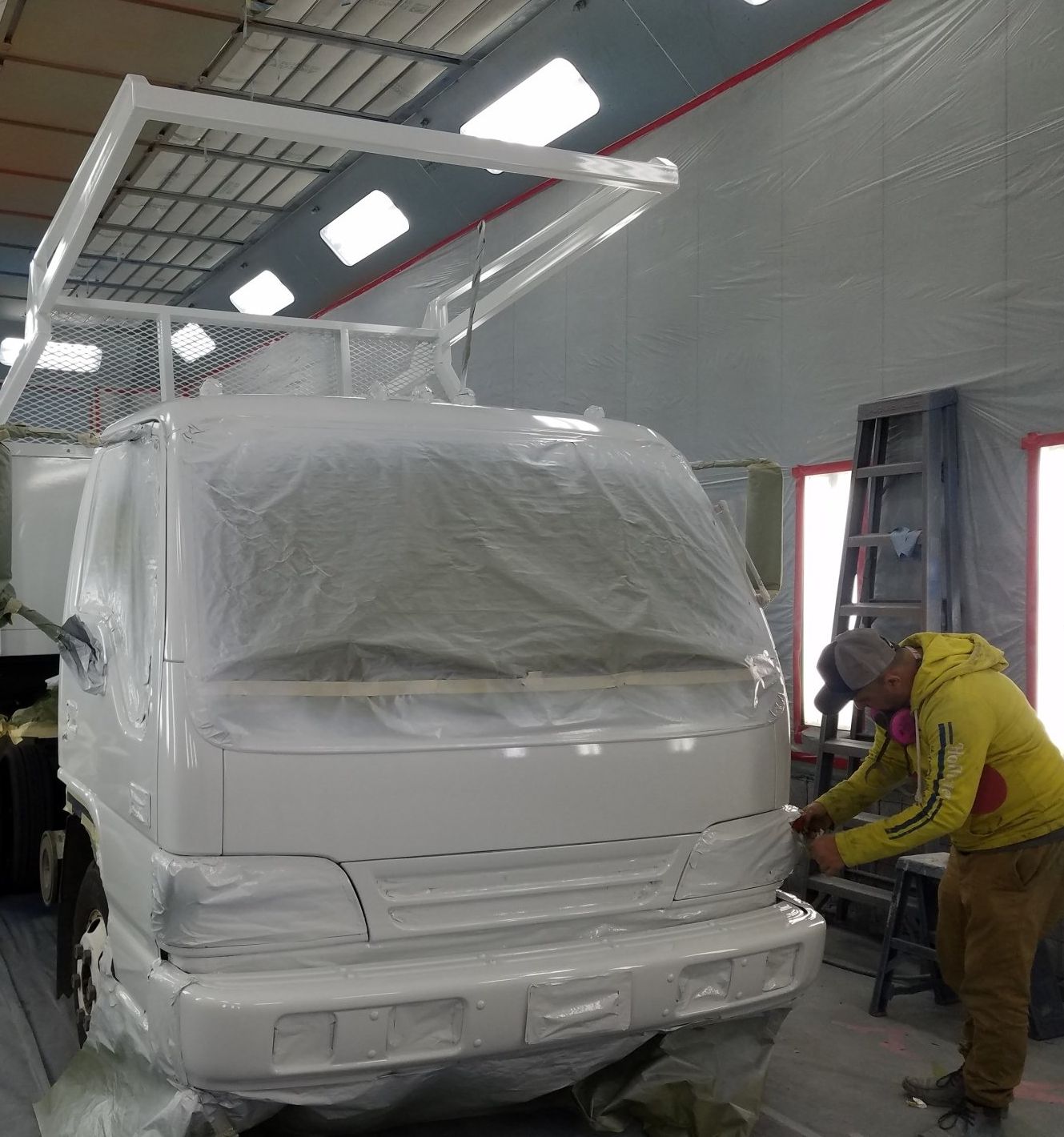 A man in a yellow jacket is painting a white truck