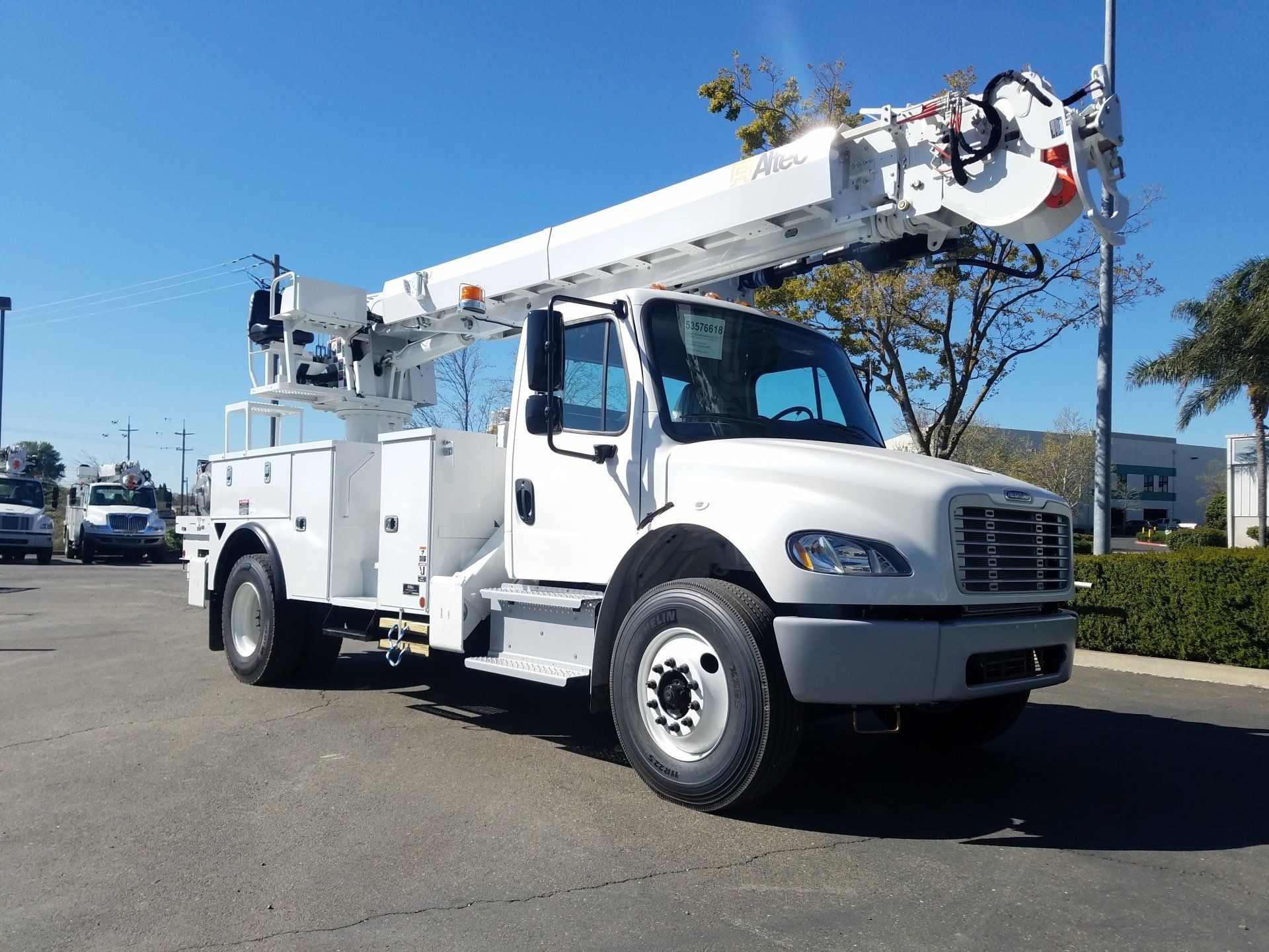 A white truck with a crane on top of it is parked in a parking lot.