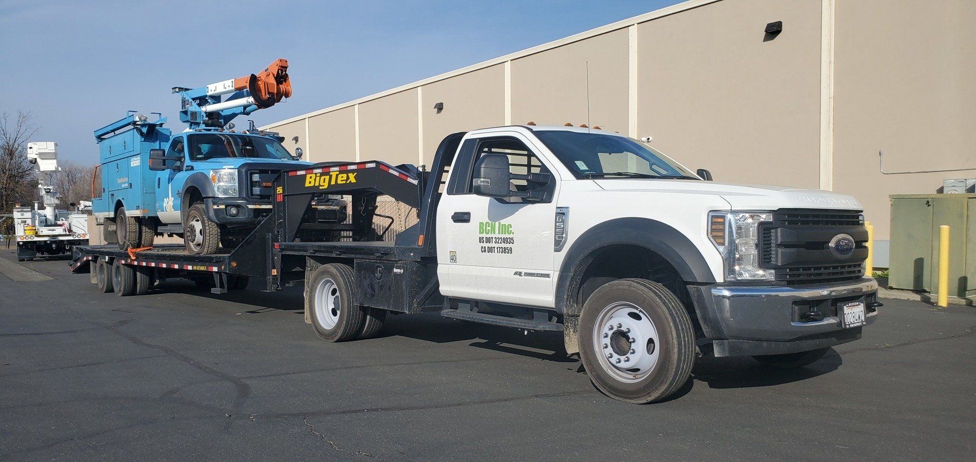 A white tow truck with a crane on the back is parked in front of a building.