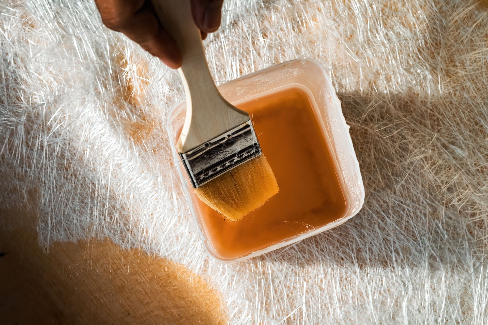 A person is holding a brush over a container of paint.