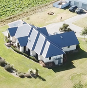 An aerial view of a modern white house with a dark blue roof, surrounded by green grass and a paved driveway.