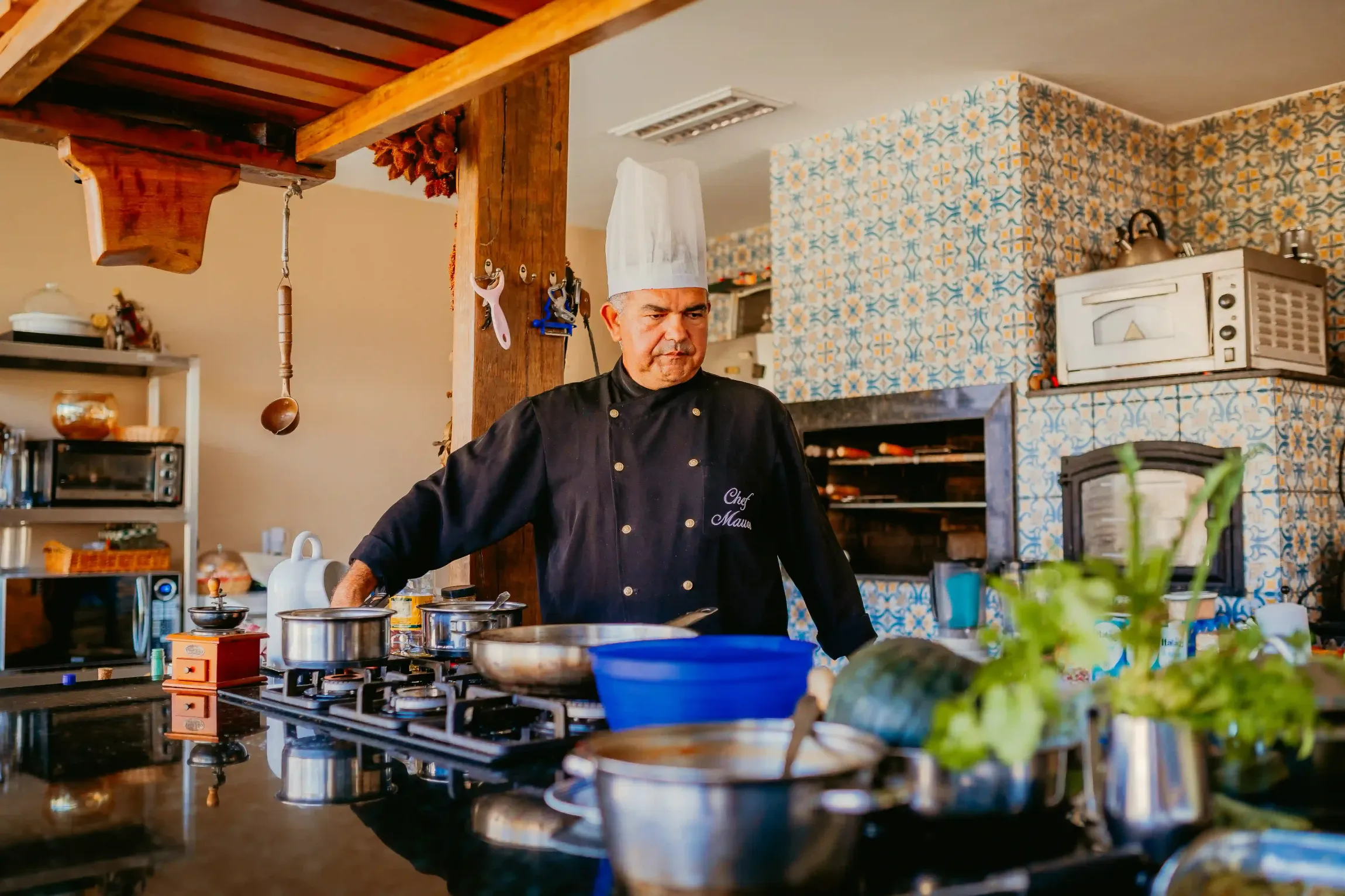Um homem com chapéu de chef está cozinhando em uma cozinha.-Pousada-Recanto-do-Chef