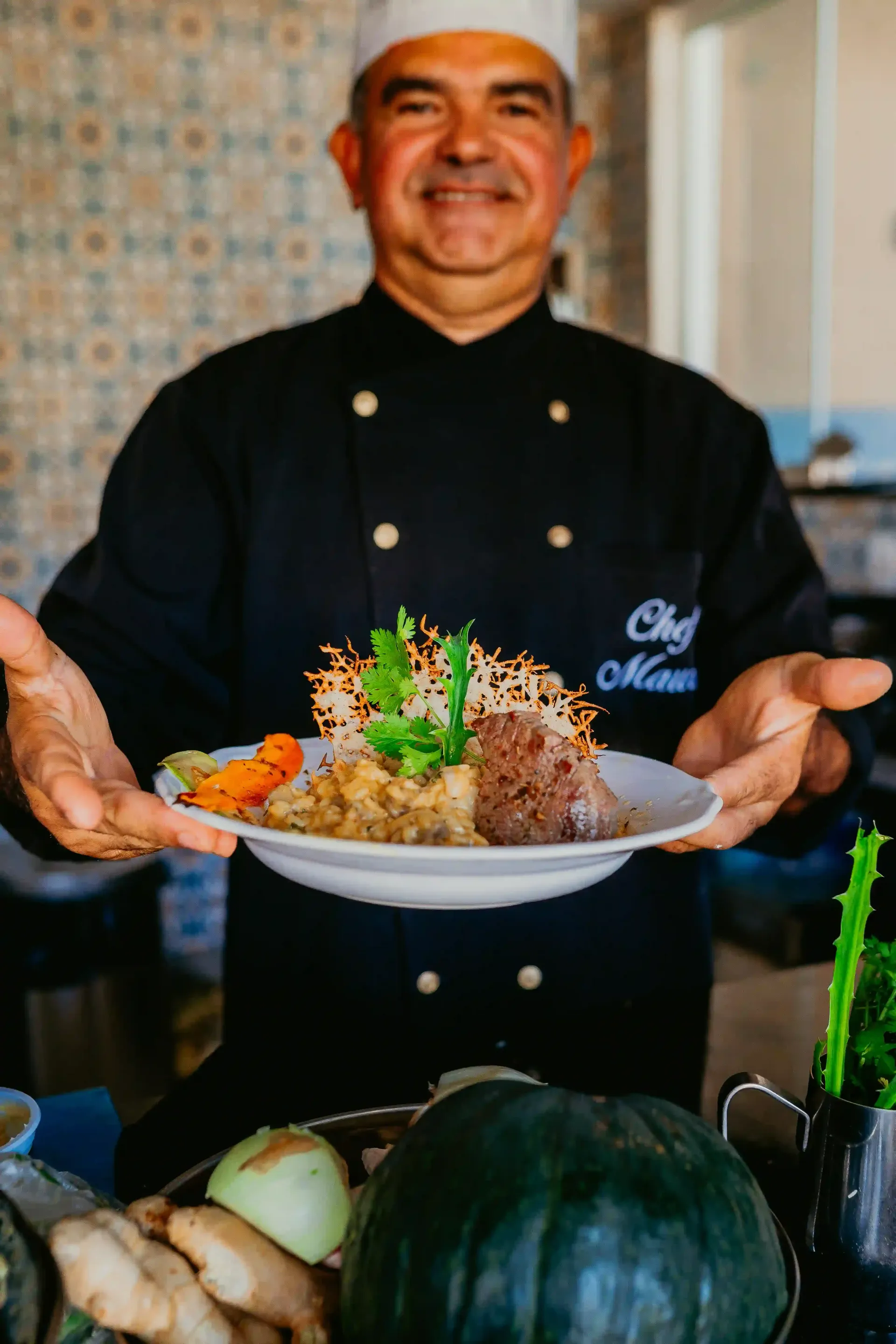 Um chef está segurando um prato de comida em suas mãos.-Pousada-Recanto-do-Chef