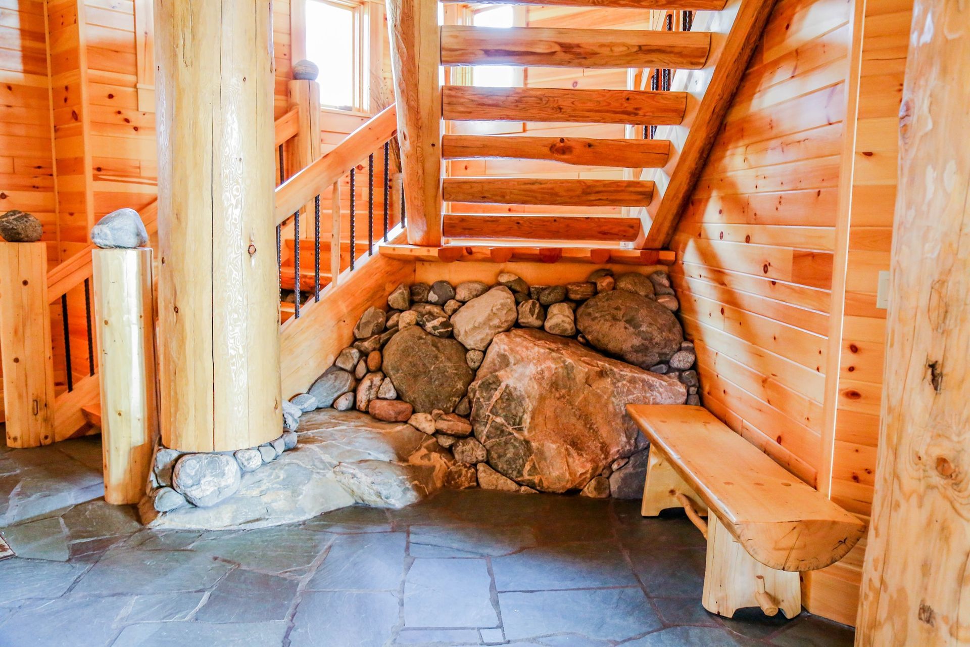 Rustic wooden stairway with log walls, stone base, and slate floor indoors