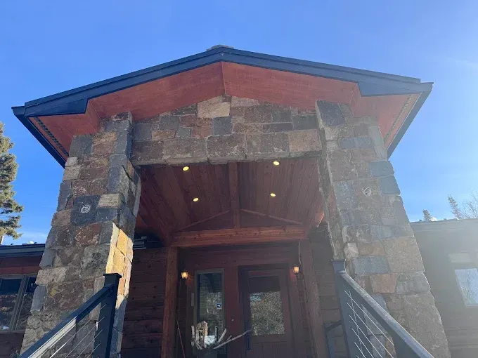 Stone lodge entrance with red roof and wooden doors under a bright blue sky