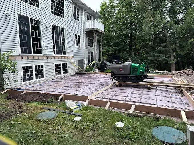Backyard deck under construction beside a house, with framing and a green machine on top.