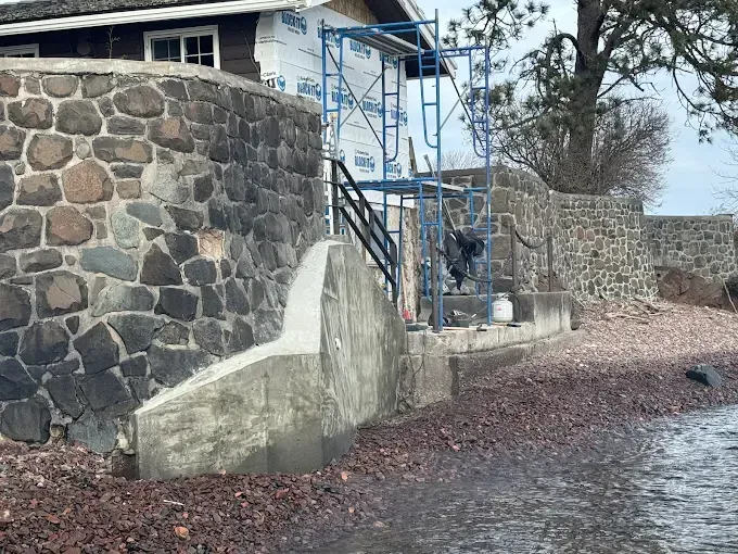 Stone retaining wall and concrete stairs beside a house under construction with blue scaffolding.