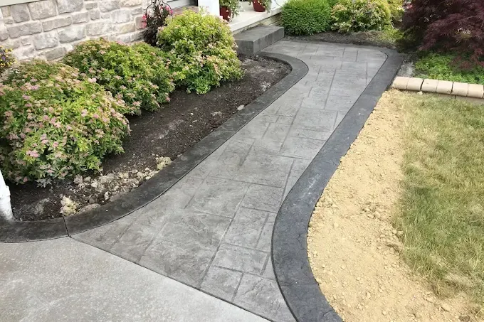 Curved gray concrete walkway beside flower beds and a lawn in a landscaped yard