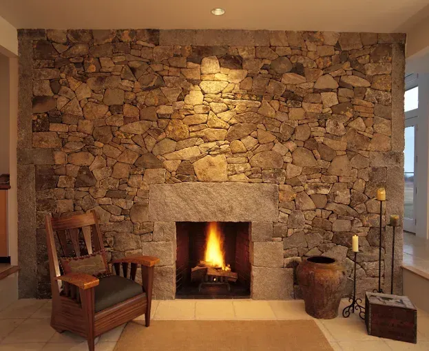 Stone fireplace in a cozy room with a lit fire, wooden chair, and candle stand
