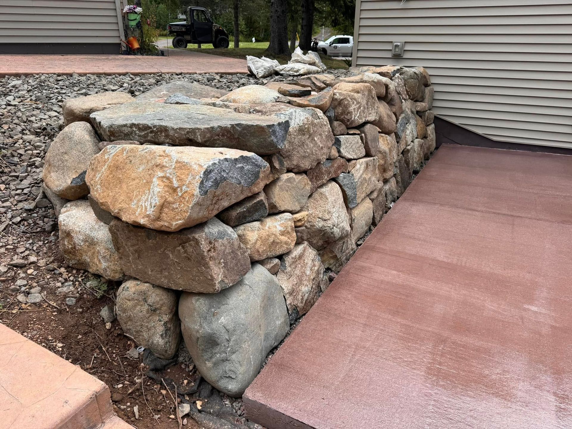 Stone retaining wall beside a red concrete driveway on a sloped residential lot