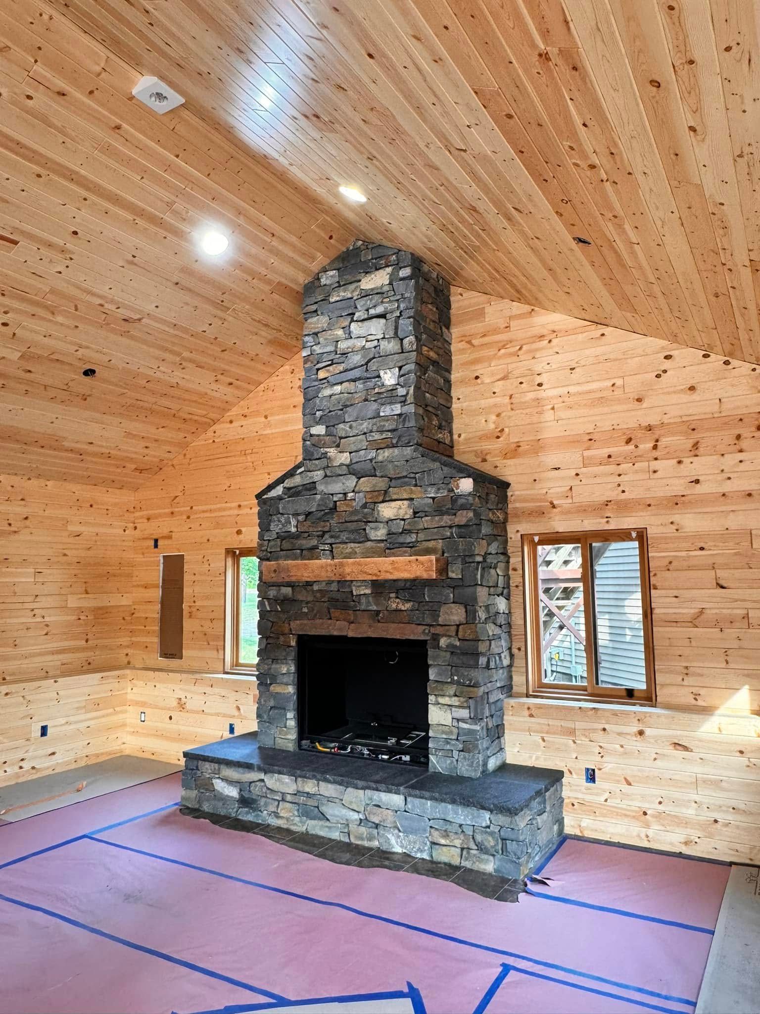 Rustic wood-paneled room with a large stone fireplace and vaulted ceiling under construction