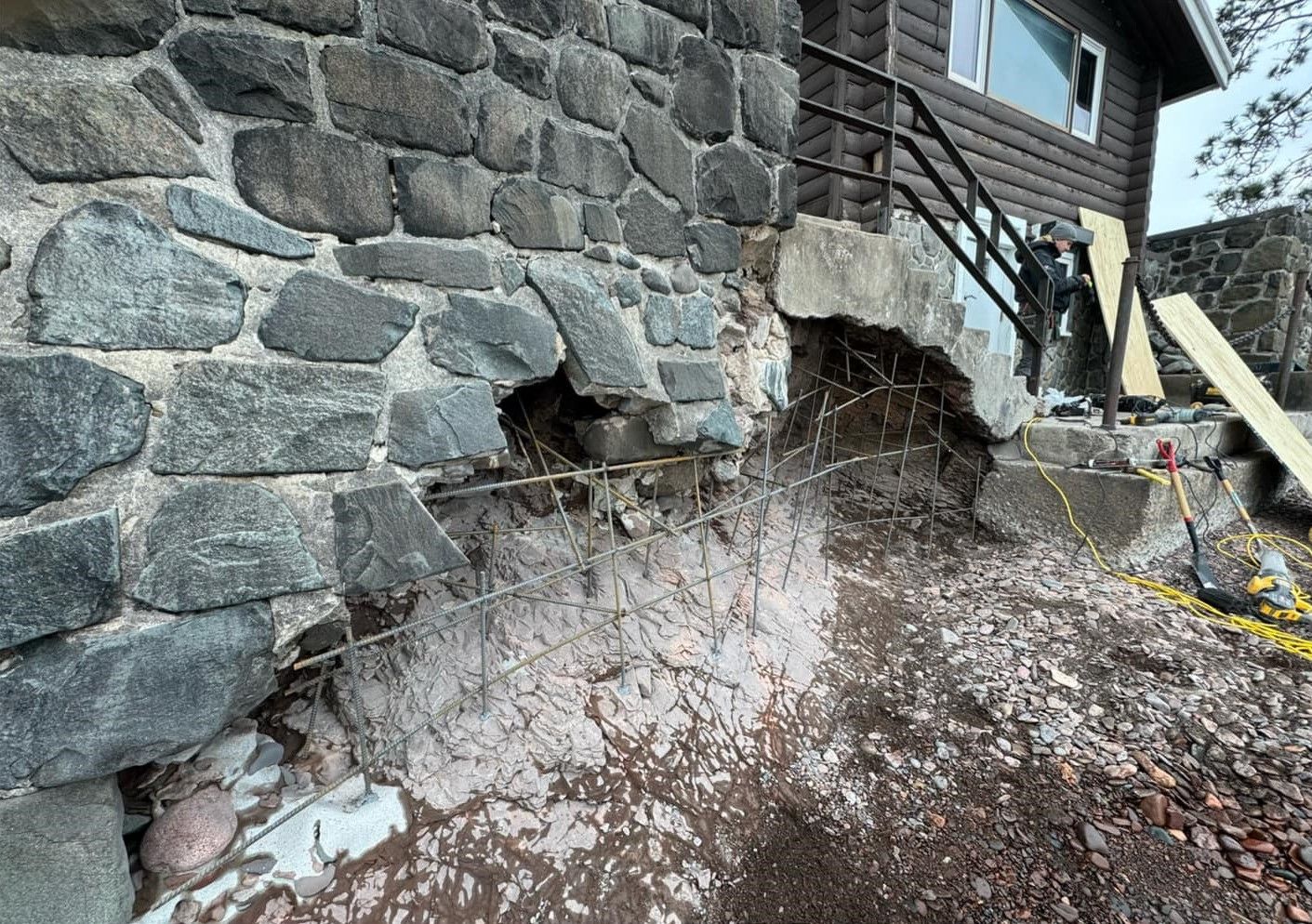 Stone house foundation with a large hole and exposed soil damage near the wall