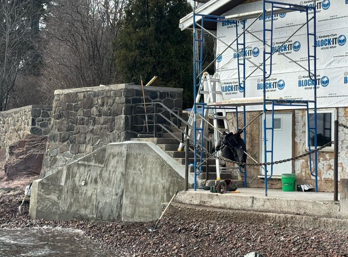 Stone stairs and retaining wall beside a house under construction, with scaffolding and workers near the entrance