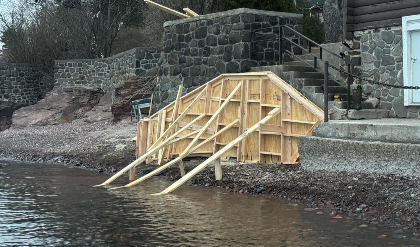 Wooden steps under construction on a rocky shoreline beside calm water and stone retaining walls