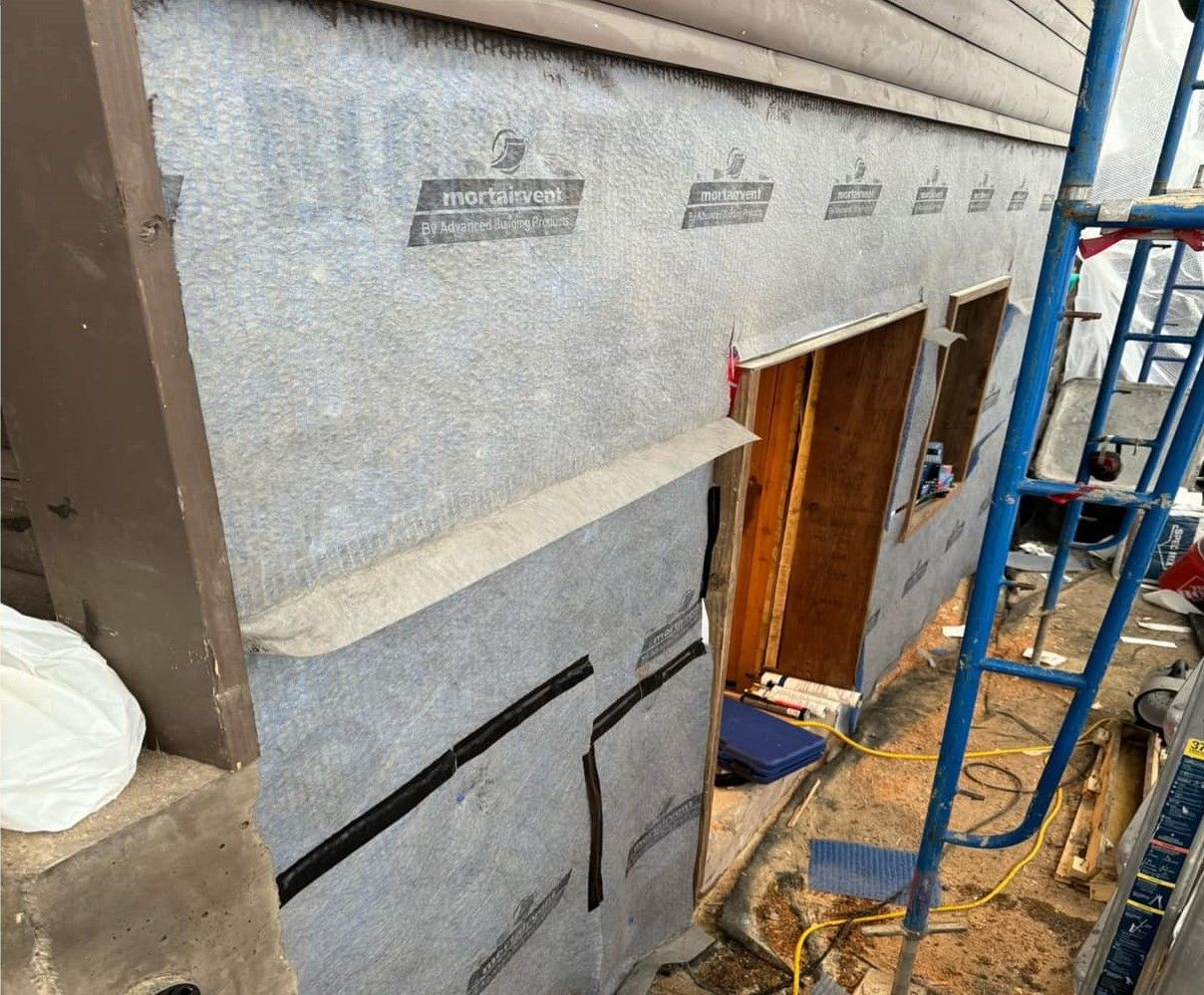House exterior under construction with gray siding, open doorway, and blue scaffolding