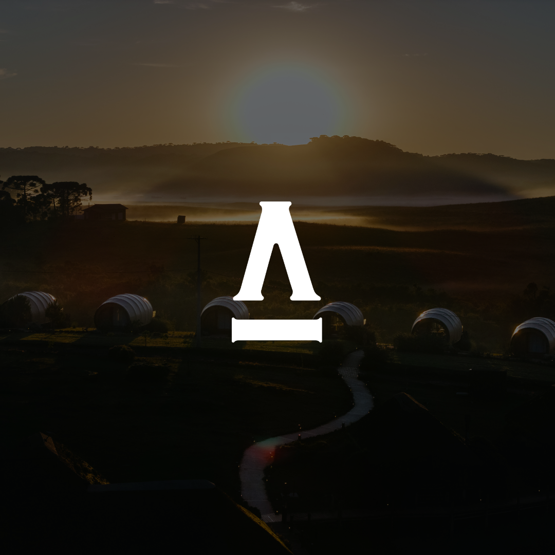 Nascer do sol sobre colinas enevoadas com um logotipo branco brilhante centralizado acima de tendas escuras e um caminho sinuoso.