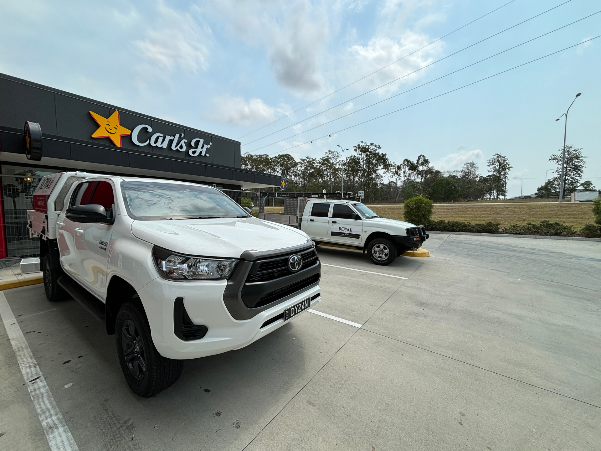 Two white trucks are parked in front of a car dealership.